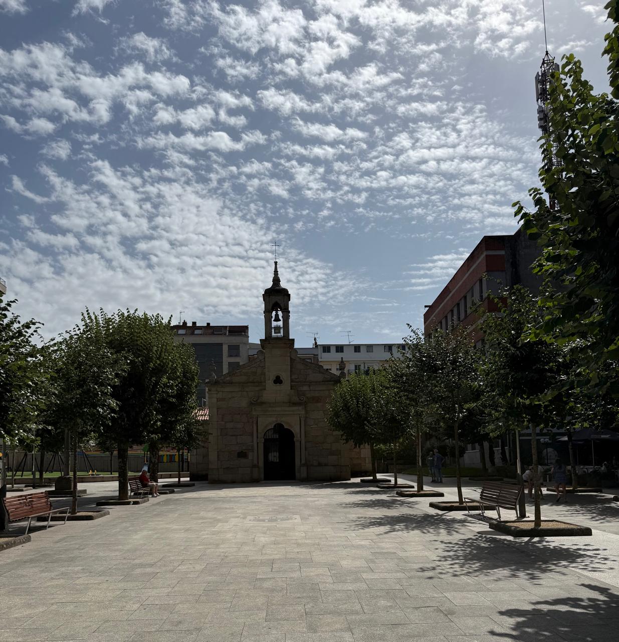Pequena capela de pedra em praça arborizada