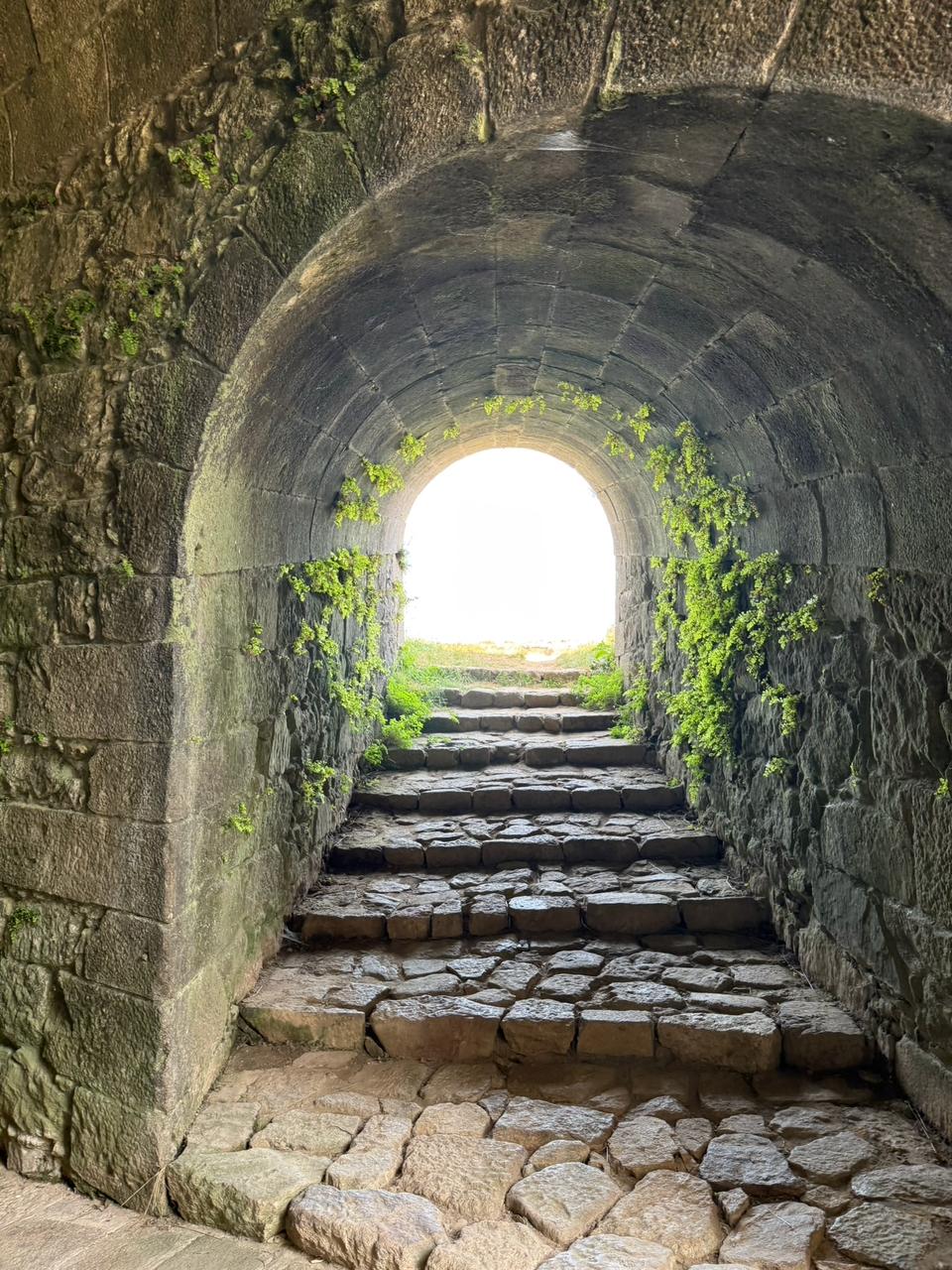 Passagem de pedra em arco com escadas antigas e luz ao fundo